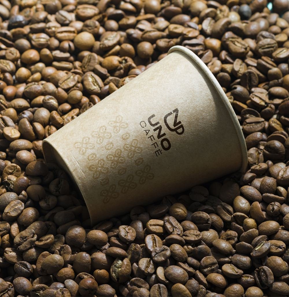 Copo Uno Caffè deitado sobre grãos de café torrados